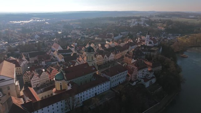 Cinematic point of view drone capture flying over the red rooftops and narrow alleyways of Neuburg an der Donau residential city showcasing the prominent palace church tower