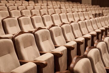Fototapeta premium Rows of empty beige velvet theater seats in a dimly lit auditorium