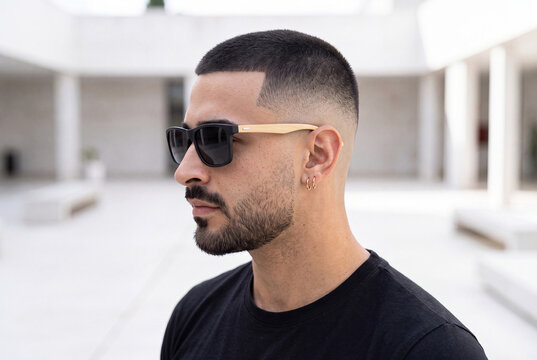 Side profile of a stylish man with a buzz cut fade and beard wearing wooden sunglasses