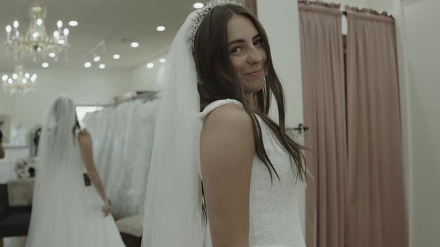 A young woman is trying on wedding dresses while her mother observes in the background, St. George, Utah