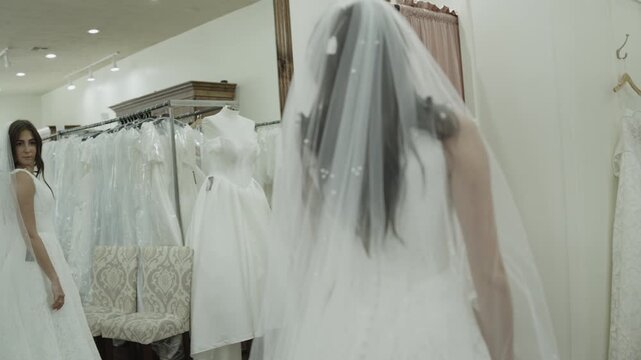 A young woman is trying on wedding dresses while her mother observes in the background, St. George, Utah