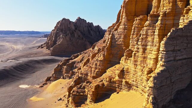 Stunning yardang landform with majestic sandstone cliffs under a clear blue sky in Xinjiang.