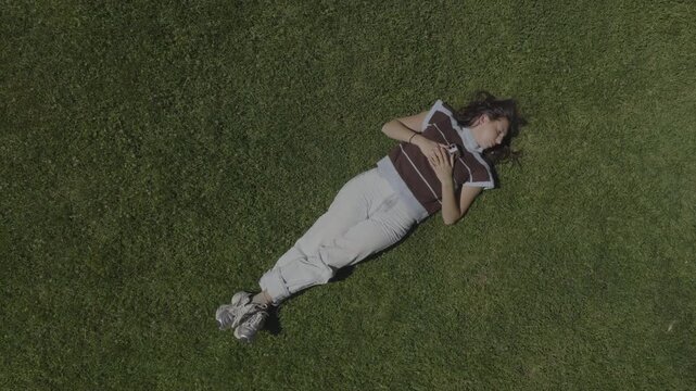An aerial flyover of a young woman asleep, laying on the grass in a park, St. George, Utah