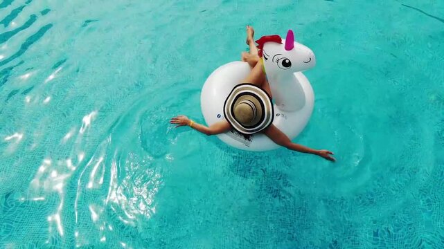 Beautiful woman on unicorn pool float in pool. Summer holidays. Aerial top view from drone
