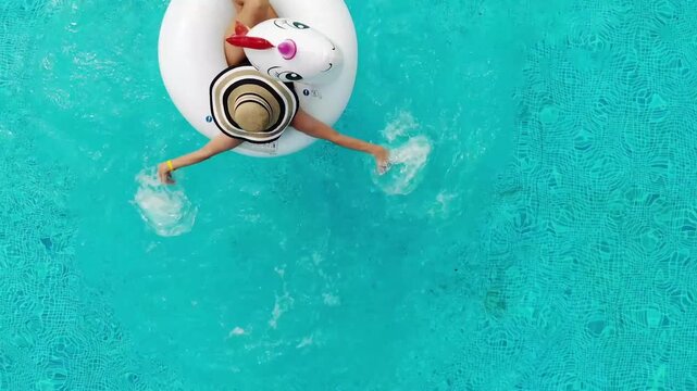 Beautiful woman on unicorn pool float in pool. Summer holidays. Aerial top view from drone
