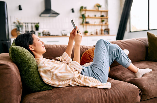 Young woman relaxing on sofa with smartphone at home.