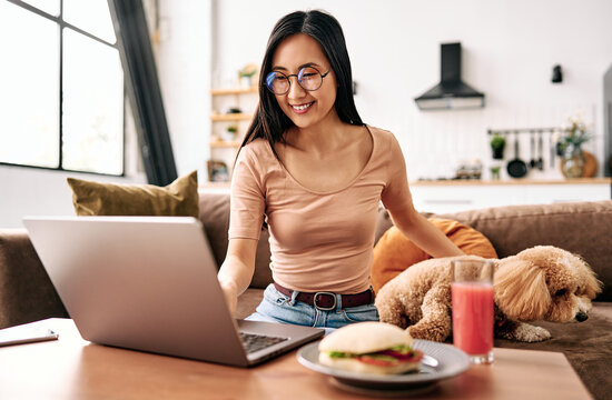Young woman using laptop at home with dog nearby.