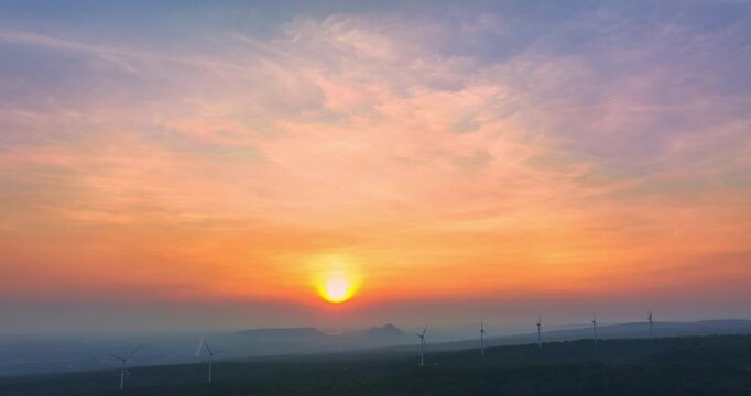 Stunning aerial scenery of sunrise above Lam Takhong Dam in Nakhon Ratchasima. where the horizon glows in soft hues. Wind turbines stand gracefully over green hills, blending nature 