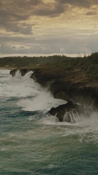 An aerial flyover vertical video of waves crashing against a rugged coastline at sunset Kauai, Hawaii