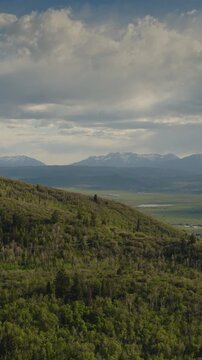 An aerial flyover vertical video of foothills near the Uintah mountains revealing a valley and farmland in the distance, Kamas, Utah
