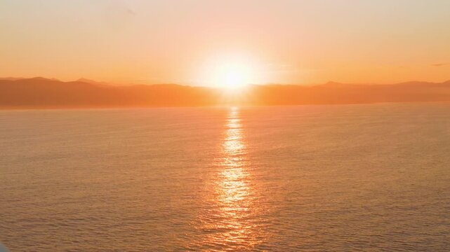 Golden hour sun setting over mountain ridge and ocean