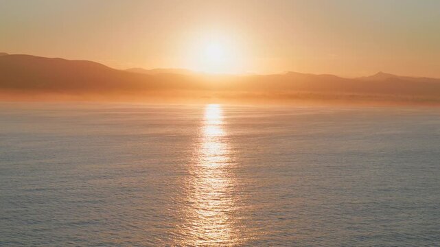 Wide angle view of a brilliant bright sun rising over a peaceful coastal marine channel.