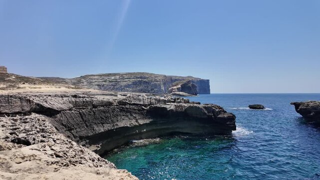 Dwejra bay, Gozo, Malta - A tranquil coastal landscape featuring a rocky coastline with clear blue skies and an expansive ocean view. Fungus rock in the background. High quality 4k footage