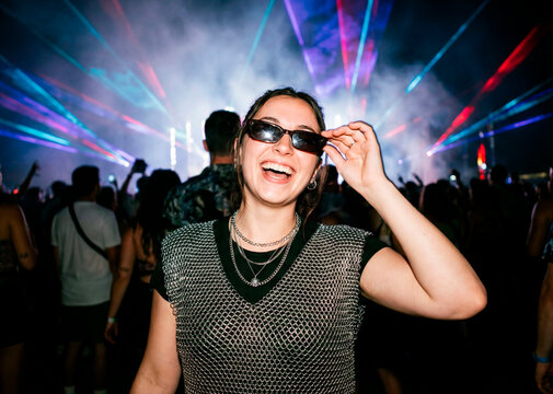 Confident young woman in a mesh top laughing under colorful lasers at a night music festival