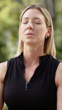 Vertical video: Cam focusing woman breathing calmly opening eyes smiling in park in zip-top, hoops