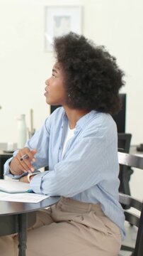 Vertical video: Writing woman in blue shirt pausing on off-camera cue in home office, holding pen