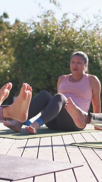 Vertical video: Anchoring band to partner foot, woman in pink tank moving legs on deck for fitness