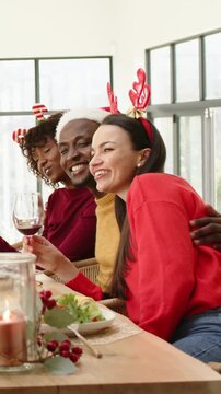 Vertical video: Smiling trio leaning in after camera prompt at table raising wine, wearing antlers