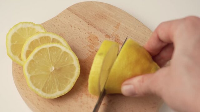 Slicing fresh lemon into thin slices on wooden cutting board
