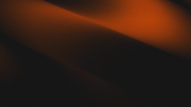 Abstract orange light glow on dark background. Smooth flowing wave movement on dark surface with golden illumination and shadows