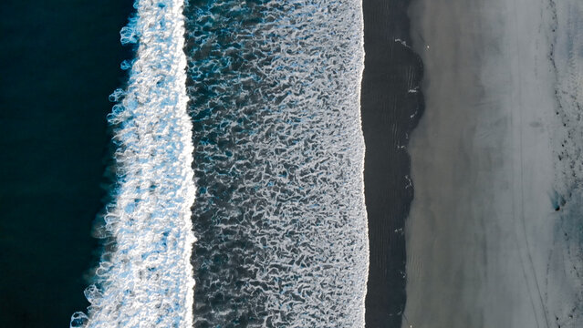 Aerial view of ocean waves crashing onto a dark sand beach in California, United States.