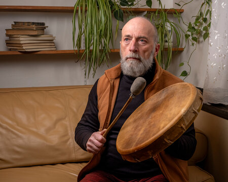 senior man is playing a native American style, shaman drum with a beater at home, lifestyle and hobby concept