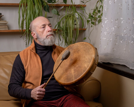 senior man is playing a native American style, shaman drum with a beater at home, lifestyle and hobby concept
