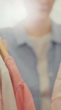 A woman in oversized clothes walks the bright store aisles during a sale, scanning racks of discounted fashion items, handling each piece carefully while keeping up with seasonal style trends