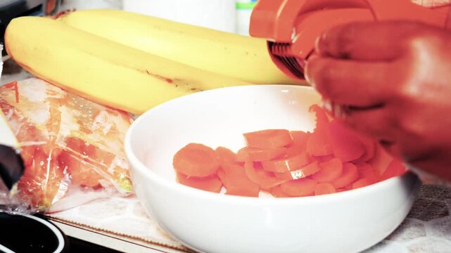 Hands slicing fresh carrots with orange multi blade kitchen gadget