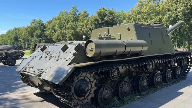 Military Tank on Display: A powerful military tank, likely a self-propelled artillery piece, is showcased in an outdoor setting with trees and clear sky in the background.