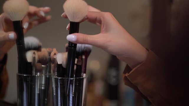 Hand of makeup artist rotating jar with brushes to choose the right tool, selecting one and not returning it.
