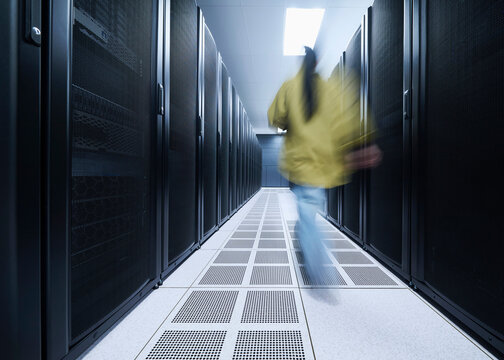 Data Center Engineer Walking Through Server Aisles