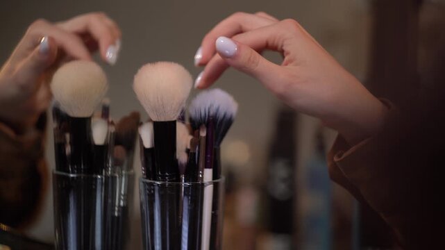 Hand of makeup artist rotating jar with brushes, touching several different brushes before finally selecting the right one and removing it from jar.
