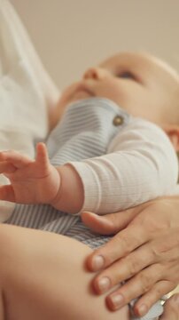 A young mother gently rocks her baby in a softly lit nursery, cradling the infant in her arms. The routine of maternal care and tenderness is present as she calms the child for sleep