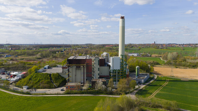 Aerial view of MVA Hamm owner-GmbH waste incineration plant with its tall chimney and industrial site surrounded by green fields and rural landscape in Hamm, Nordrhein-Westfalen, Germany.