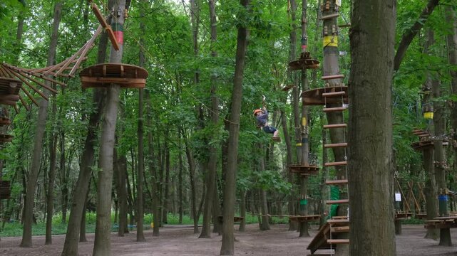 Child sliding on a zip line in an outdoor forest adventure park during summer