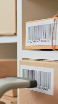 An employee of a postal company uses a scanner to read a barcode on a cardboard box in a warehouse, recording parcel data for shipping to customers, managing logistics and parcel inventory