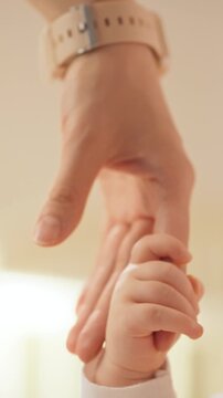 Close-up of a mother's hands holding an infant, the baby's fingers clasp the mother's fingers, showing early caregiving. The tactile contact highlights sensory bonding in newborn care
