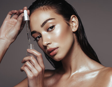Beautiful woman with wet glowing skin holding a serum dropper and bottle