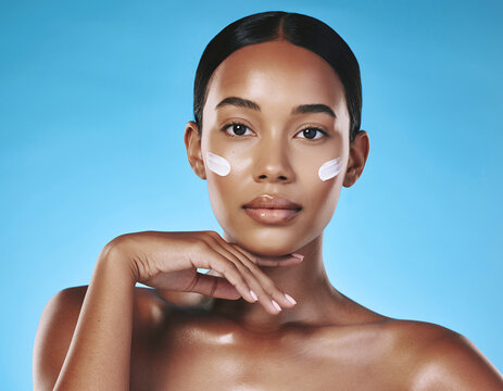 Radiant Young Woman with Skincare Cream on Cheeks over a Solid Blue Setting