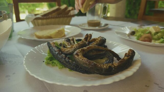 Person Squeezing Fresh Lemon Juice On Grilled Eel Fish Dish. Seafood Delicacy Plate. Mediterranean Dinner