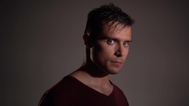 Young man standing almost in profile, then turning head and body to front, staring intently into camera with concentrated, focused expression.
