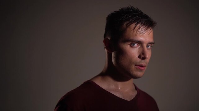 Young man standing still, turning only head and gaze toward camera with suspicious, confused expression. 
