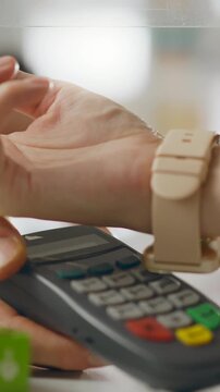 In a modern pharmacy, a buyer receives a payment terminal from the pharmacist, uses a smart watch to finalize the purchase of medicines, a digital checkout workflow in a busy setting