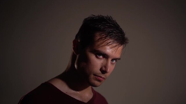 Young man turning only head and gaze toward camera with arrogant, challenging, psychological pressure expression. 
