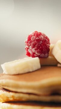 In the kitchen, a cook arranges fresh raspberries on a stack of golden pancakes on a plate, preparing fruit and berry pancakes tomorrow. A large pancake and raspberry plan