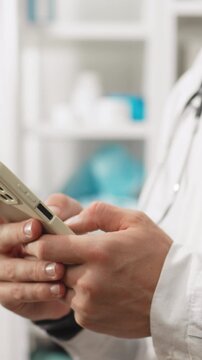 Male doctor in clinic uniform stands in doctor's office, holding modern telephone. The moving camera captures him operating the phone, linking it to body diagnostics and routine health communication