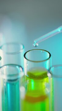 Inside a laboratory, a researcher holds a pipette and releases a clear liquid into a glass test tube, the drop captured in close view, a controlled step in scientific experimentation