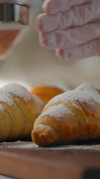 Pastry chef in culinary department dusts fresh European baked goods with fine layer of powdered sugar, demonstrating specialist technique and supporting consistent manufacture in professional kitchen