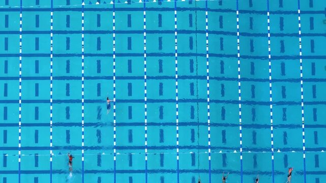 Drone top view of outdoor sports swimming pool with swimmers gliding along lane markers. Healthy lifestyle and water sport activities.